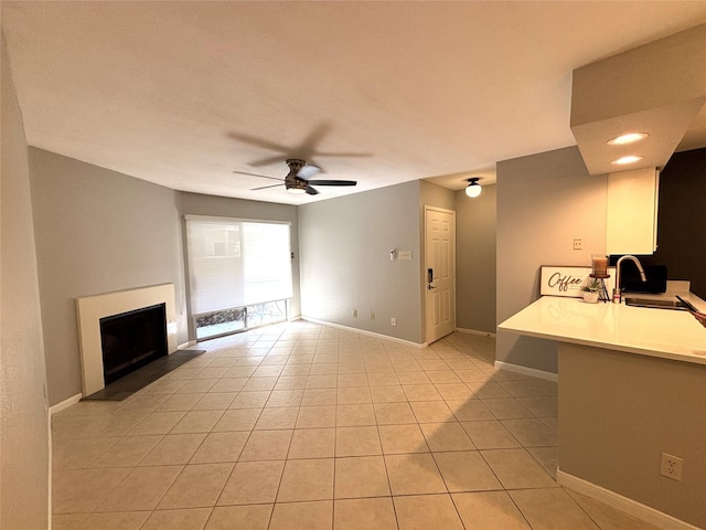 unfurnished living room featuring a fireplace with raised hearth, a ceiling fan, light tile patterned flooring, a sink, and baseboards