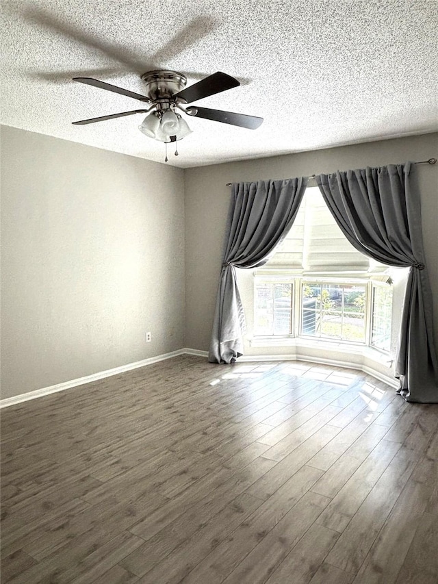 empty room featuring ceiling fan, a textured ceiling, baseboards, and dark wood-type flooring