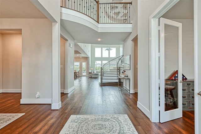 entrance foyer featuring dark wood-style floors, a high ceiling, baseboards, and stairs