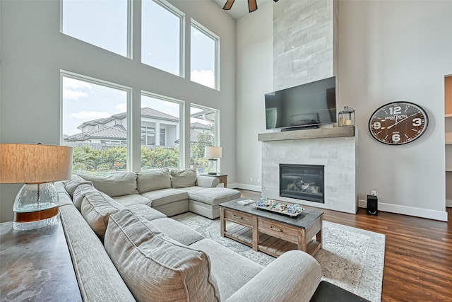 living area with a high ceiling, a fireplace, baseboards, and wood finished floors