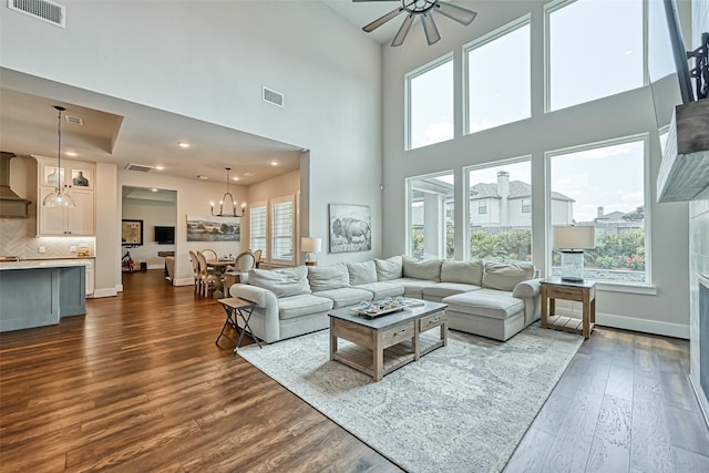 living area featuring dark wood-style floors, ceiling fan with notable chandelier, visible vents, and baseboards