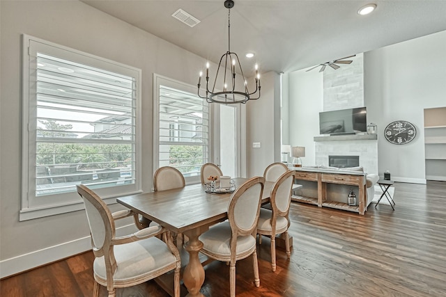 dining area featuring visible vents, wood finished floors, a tile fireplace, baseboards, and ceiling fan with notable chandelier