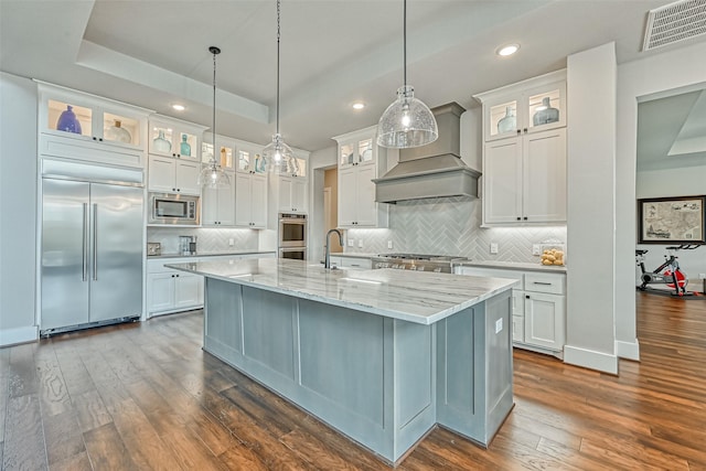 kitchen featuring built in appliances, dark wood-type flooring, visible vents, a raised ceiling, and custom range hood