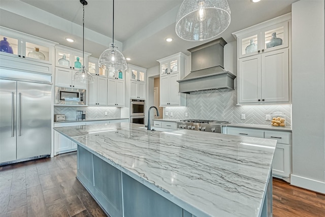 kitchen with built in appliances, a sink, white cabinets, custom exhaust hood, and dark wood finished floors