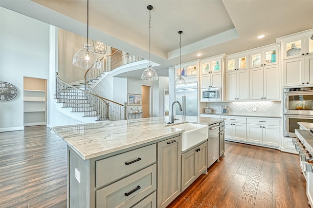 kitchen with pendant lighting, dark wood finished floors, a raised ceiling, a sink, and built in appliances