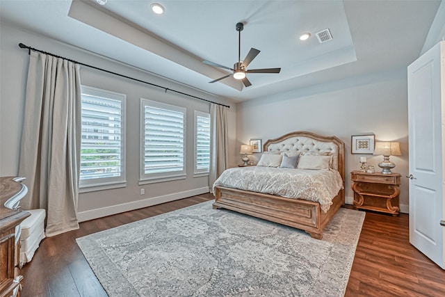 bedroom featuring a tray ceiling, dark wood finished floors, recessed lighting, visible vents, and baseboards