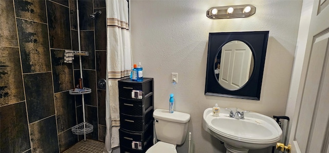 full bath featuring a sink, a textured wall, a tile shower, and toilet