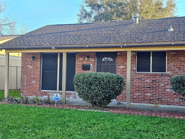 property entrance with roof with shingles, fence, and brick siding