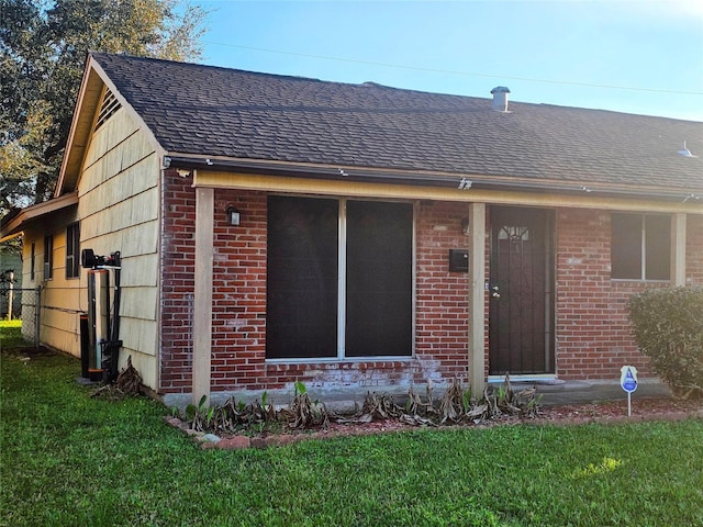 exterior space with a yard, roof with shingles, and brick siding