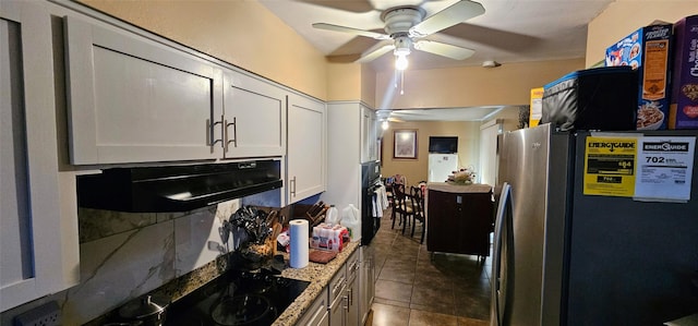 kitchen featuring dark tile patterned floors, a ceiling fan, freestanding refrigerator, white cabinetry, and under cabinet range hood