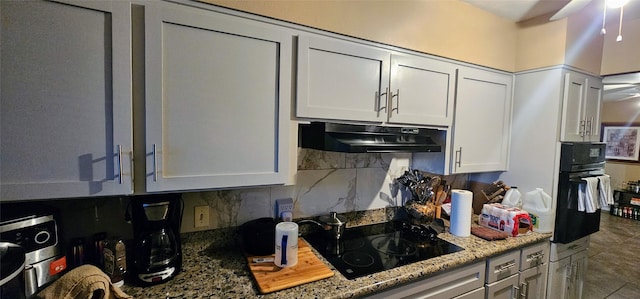 kitchen with tasteful backsplash, light stone countertops, under cabinet range hood, black appliances, and white cabinetry