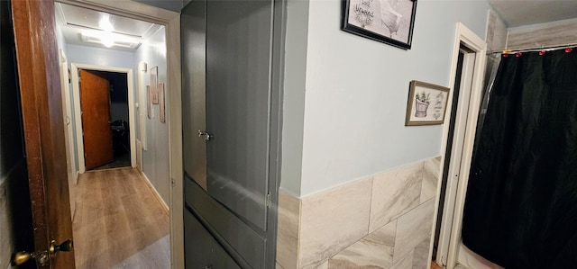 hall with light wood-type flooring, attic access, and tile walls