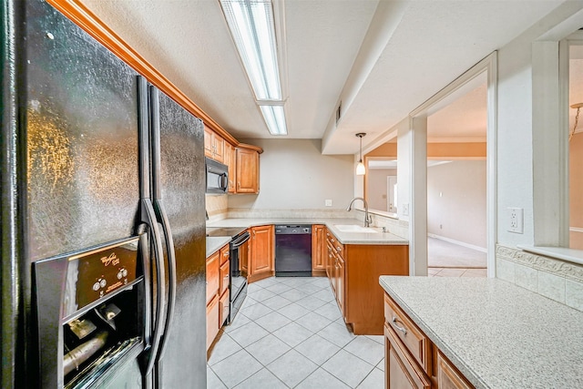 kitchen with light tile patterned floors, light countertops, brown cabinetry, a sink, and black appliances