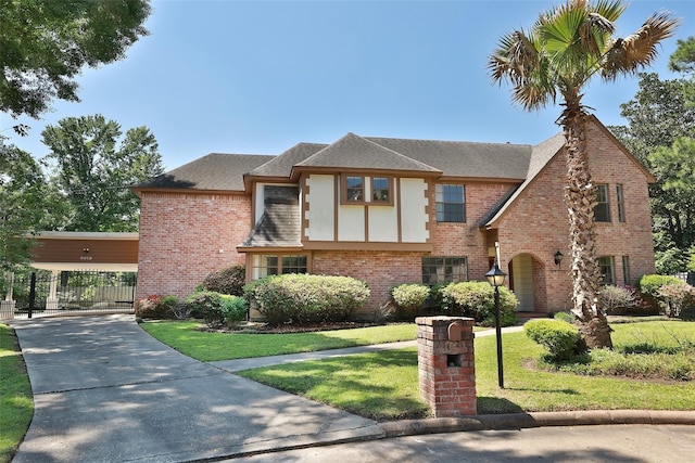 tudor house featuring a gate, brick siding, a front lawn, and roof with shingles