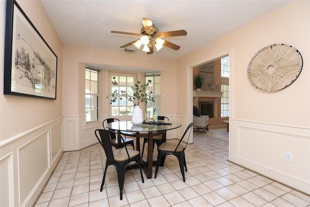 dining area with wainscoting, a fireplace with raised hearth, visible vents, and light tile patterned floors