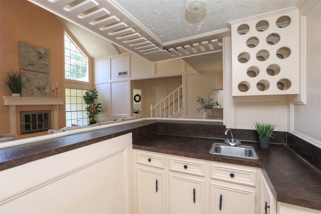 kitchen with lofted ceiling, a textured ceiling, a sink, dark countertops, and a glass covered fireplace