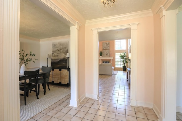 corridor with light tile patterned floors, decorative columns, baseboards, ornamental molding, and a textured ceiling