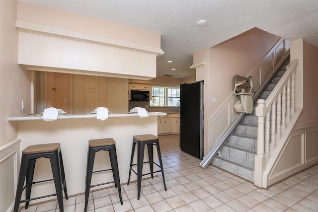 kitchen featuring a breakfast bar, a decorative wall, a peninsula, and black appliances