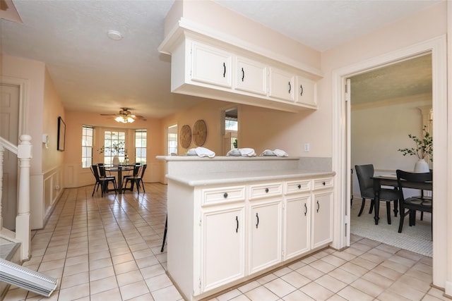 kitchen with light tile patterned floors, ceiling fan, a peninsula, light countertops, and white cabinetry