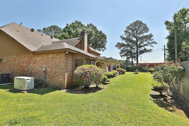 view of side of property featuring a chimney, fence, cooling unit, a yard, and brick siding