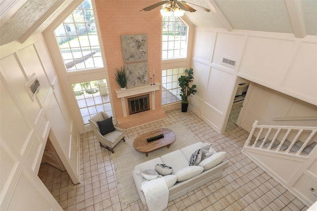 living room featuring beam ceiling, a glass covered fireplace, visible vents, and a decorative wall