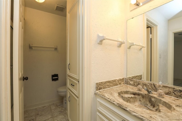 bathroom featuring toilet, vanity, visible vents, and baseboards