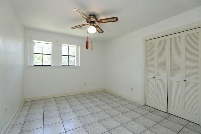 unfurnished bedroom featuring a closet, light tile patterned flooring, a ceiling fan, and baseboards