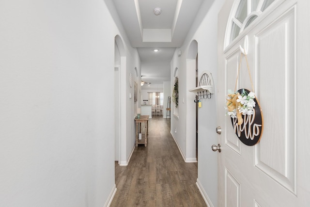 corridor featuring arched walkways, dark wood-type flooring, and baseboards