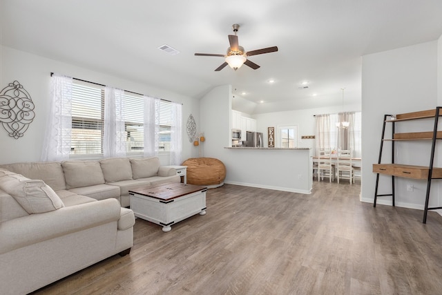 living area with lofted ceiling, visible vents, wood finished floors, baseboards, and ceiling fan with notable chandelier