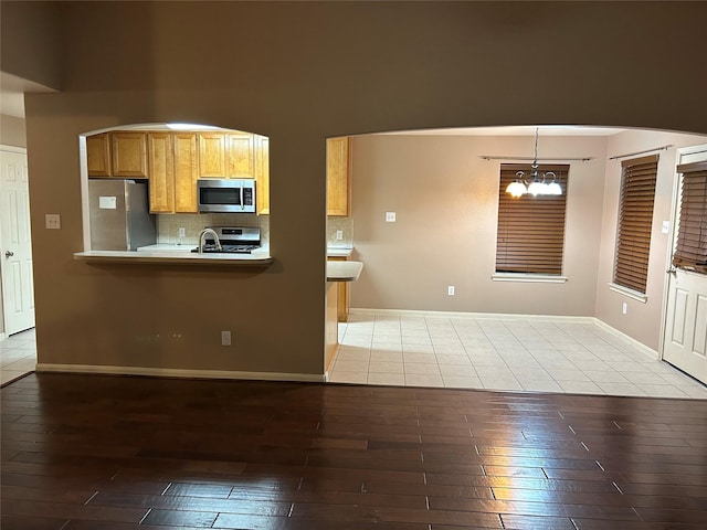 kitchen featuring stainless steel appliances, wood-type flooring, decorative backsplash, and an inviting chandelier