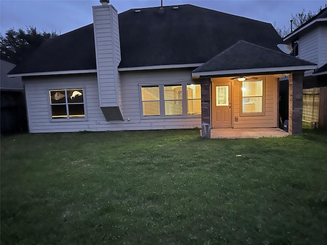 rear view of house with ceiling fan, a yard, a chimney, and a patio