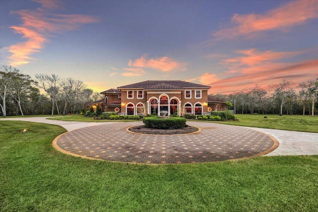 back of property featuring a tiled roof, curved driveway, and a lawn