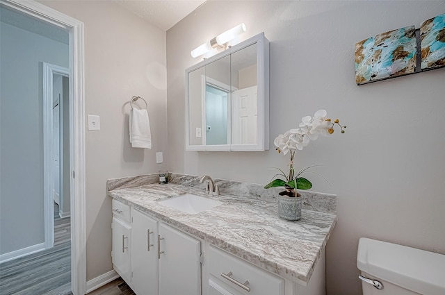 half bath with wood finished floors, vanity, toilet, and baseboards