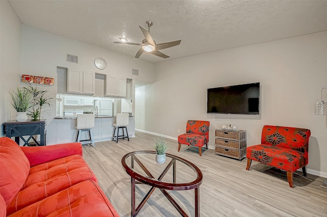 living area featuring light wood-style flooring, a textured ceiling, visible vents, and a ceiling fan