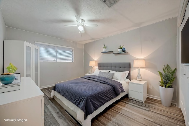 bedroom with light wood finished floors, visible vents, a ceiling fan, a textured ceiling, and baseboards