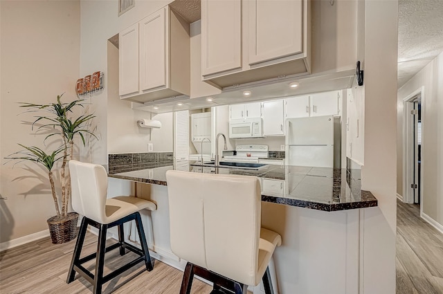 kitchen featuring white appliances, light wood finished floors, visible vents, dark countertops, and a peninsula