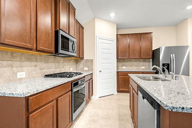 kitchen with light stone counters, stainless steel appliances, decorative backsplash, a kitchen island with sink, and a sink