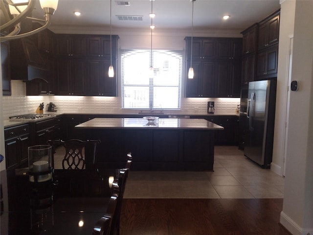 kitchen with ornamental molding, appliances with stainless steel finishes, a kitchen island, and tasteful backsplash