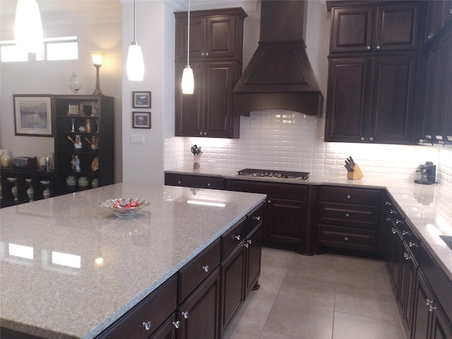 kitchen featuring a center island, light stone countertops, custom exhaust hood, gas cooktop, and backsplash