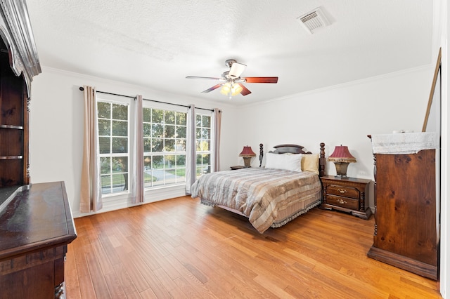 bedroom featuring visible vents, crown molding, a textured ceiling, and light wood finished floors