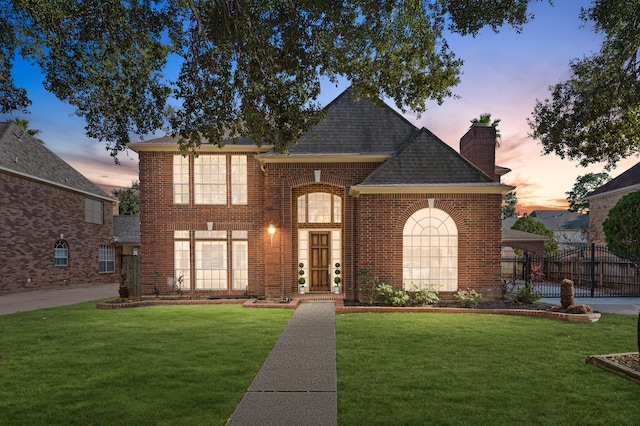 view of front facade with brick siding, a chimney, a shingled roof, a lawn, and fence