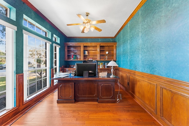 unfurnished office featuring a ceiling fan, wainscoting, crown molding, and light wood-style flooring