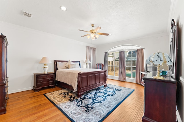 bedroom with baseboards, visible vents, a textured ceiling, crown molding, and light wood-style floors