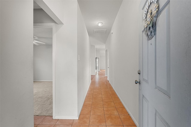 hall featuring baseboards, light tile patterned flooring, visible vents, and light colored carpet