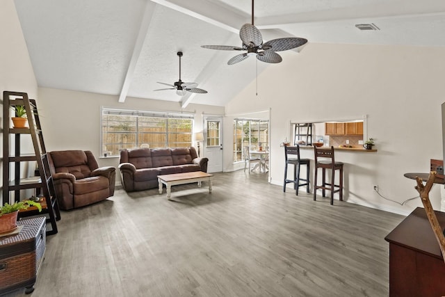 living room with beamed ceiling, wood finished floors, visible vents, and a healthy amount of sunlight