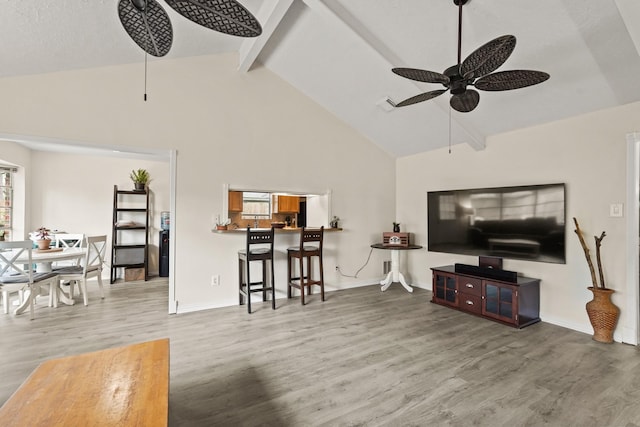 living area featuring beam ceiling, a ceiling fan, wood finished floors, high vaulted ceiling, and baseboards