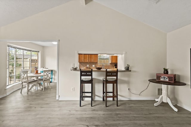 kitchen with light wood finished floors, brown cabinetry, backsplash, and a kitchen breakfast bar