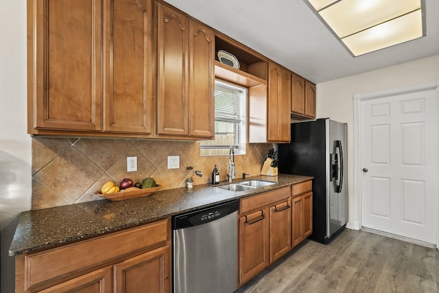 kitchen featuring stainless steel appliances, light wood-type flooring, a sink, and dark stone countertops