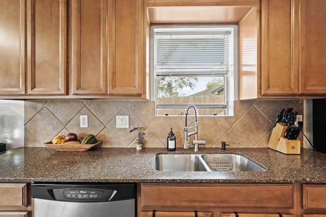 kitchen featuring decorative backsplash, dark stone counters, a sink, and stainless steel dishwasher