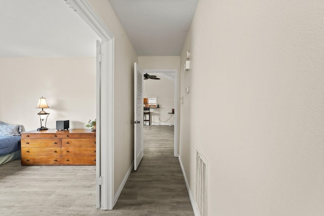 hallway featuring baseboards, visible vents, and wood finished floors